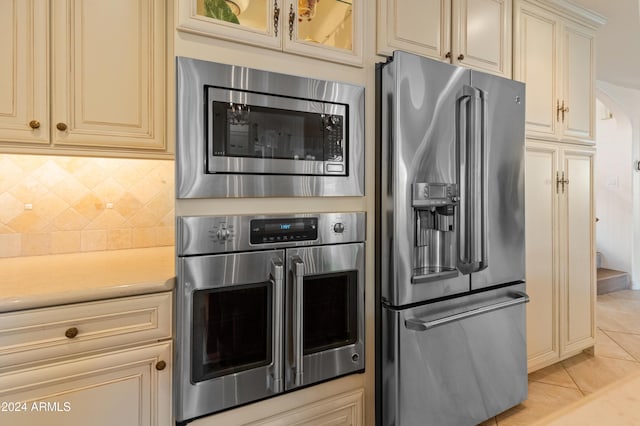 kitchen with tasteful backsplash, light tile patterned flooring, stainless steel appliances, and cream cabinetry