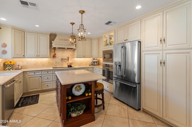 kitchen with premium range hood, hanging light fixtures, appliances with stainless steel finishes, tasteful backsplash, and a kitchen island