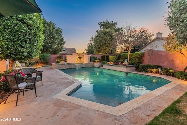 pool at dusk with a patio and exterior fireplace