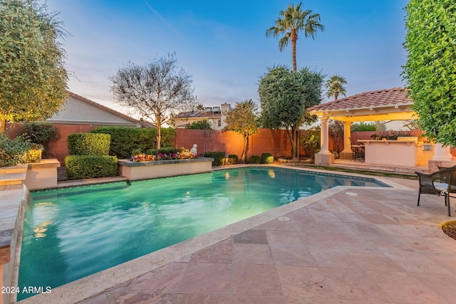 pool at dusk featuring a patio area and a bar