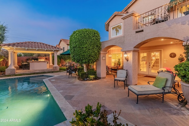 pool at dusk with an outdoor bar, exterior kitchen, a patio, and french doors