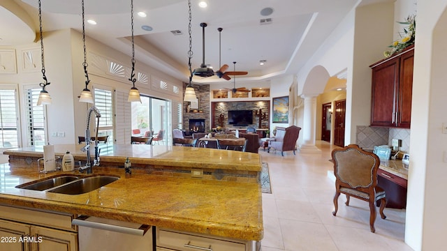 kitchen featuring pendant lighting, a raised ceiling, a stone fireplace, and ornate columns