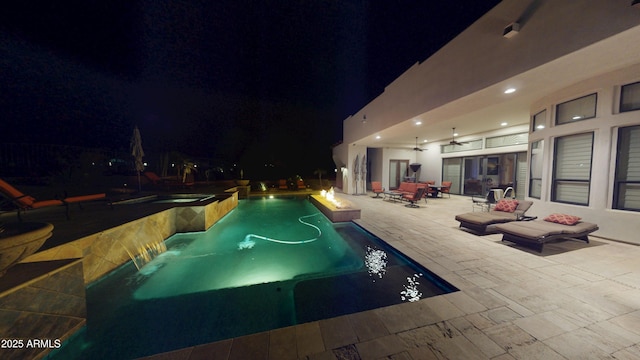 pool at night with a patio area and a pool with connected hot tub