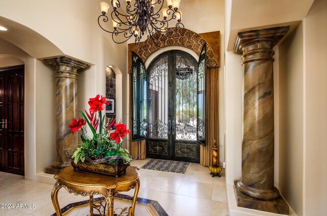 tiled foyer entrance with a notable chandelier, ornate columns, and a tray ceiling