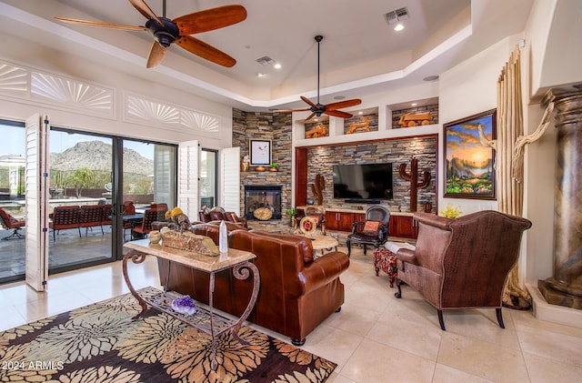 living area with light tile patterned floors, visible vents, a tray ceiling, a stone fireplace, and a mountain view