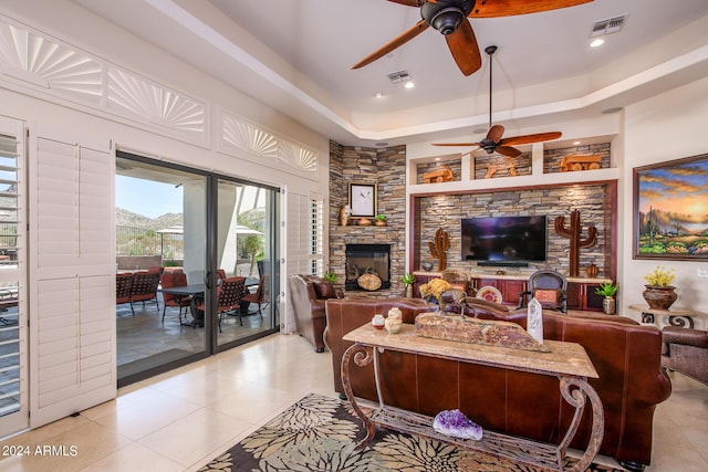 living room with a raised ceiling, visible vents, a stone fireplace, and light tile patterned flooring