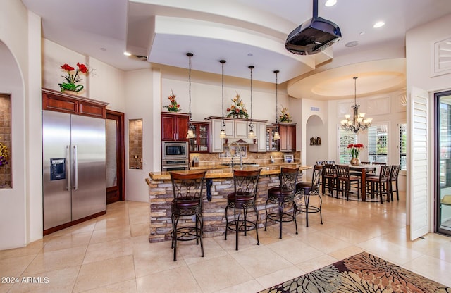 kitchen with glass insert cabinets, decorative light fixtures, built in appliances, dark brown cabinets, and backsplash