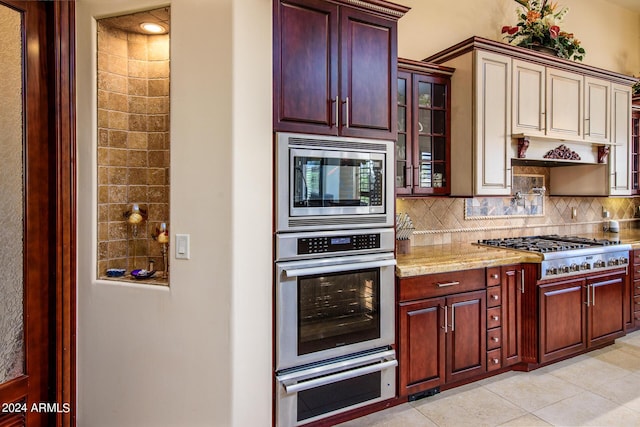 kitchen featuring stainless steel appliances, backsplash, glass insert cabinets, and light stone countertops