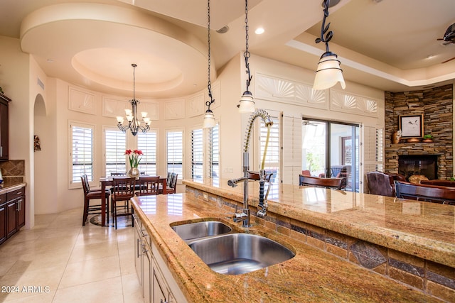 kitchen with a stone fireplace, decorative light fixtures, a raised ceiling, and light stone counters