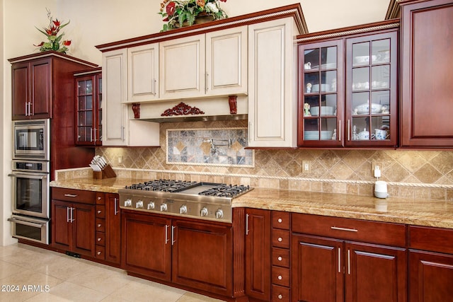 kitchen featuring light stone counters, light tile patterned flooring, stainless steel appliances, backsplash, and glass insert cabinets