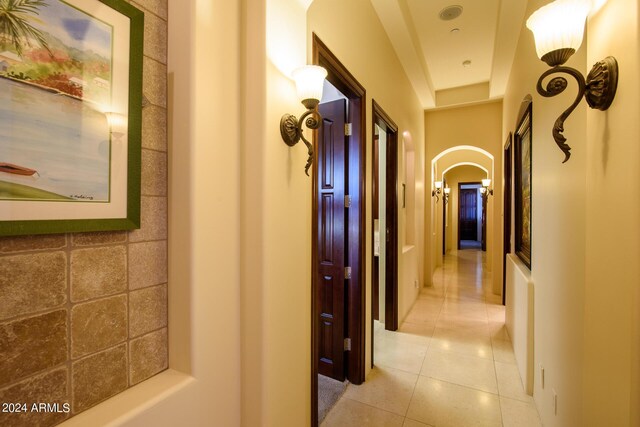 hallway featuring arched walkways and light tile patterned floors