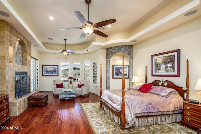 bedroom featuring visible vents, dark wood finished floors, a tile fireplace, a tray ceiling, and recessed lighting