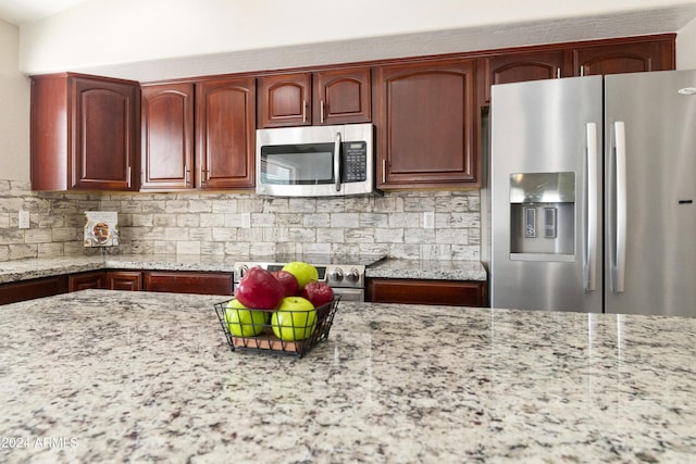 kitchen with reddish brown cabinets, stainless steel appliances, backsplash, and light stone countertops