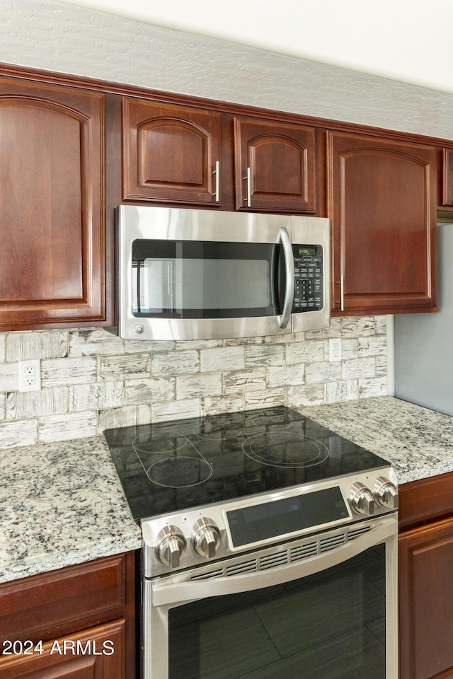 kitchen with reddish brown cabinets, light stone countertops, and appliances with stainless steel finishes