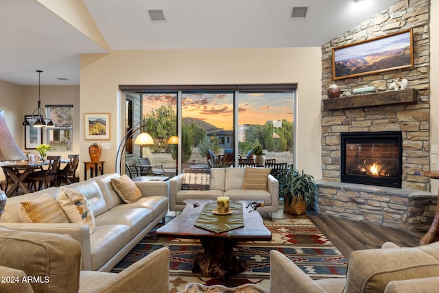 living room featuring a wealth of natural light, vaulted ceiling, a stone fireplace, and wood-type flooring