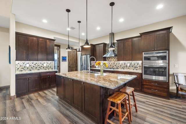 kitchen with wall chimney exhaust hood, decorative light fixtures, an island with sink, and dark hardwood / wood-style floors