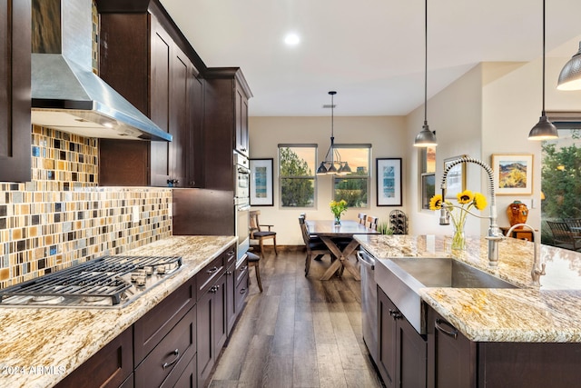 kitchen with appliances with stainless steel finishes, wall chimney range hood, pendant lighting, and dark hardwood / wood-style floors