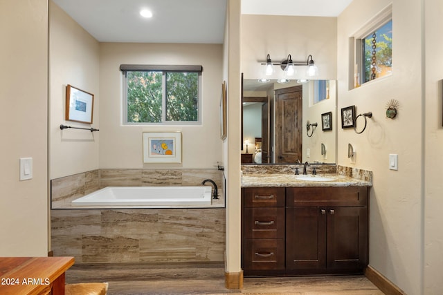 bathroom featuring a wealth of natural light, vanity, hardwood / wood-style floors, and tiled bath