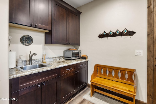 kitchen with light hardwood / wood-style flooring, light stone countertops, sink, and dark brown cabinets