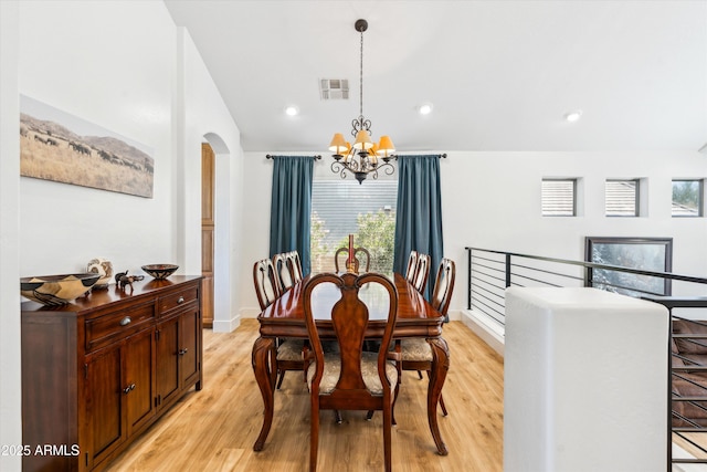 dining space with visible vents, light wood-style flooring, arched walkways, vaulted ceiling, and a notable chandelier