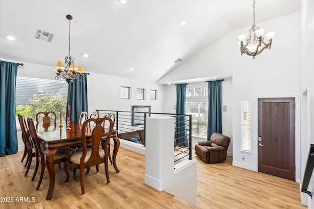 dining room with visible vents, light wood-style flooring, high vaulted ceiling, and an inviting chandelier