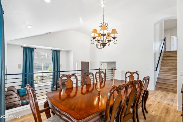 dining room featuring stairway, vaulted ceiling, light wood-style flooring, arched walkways, and a notable chandelier