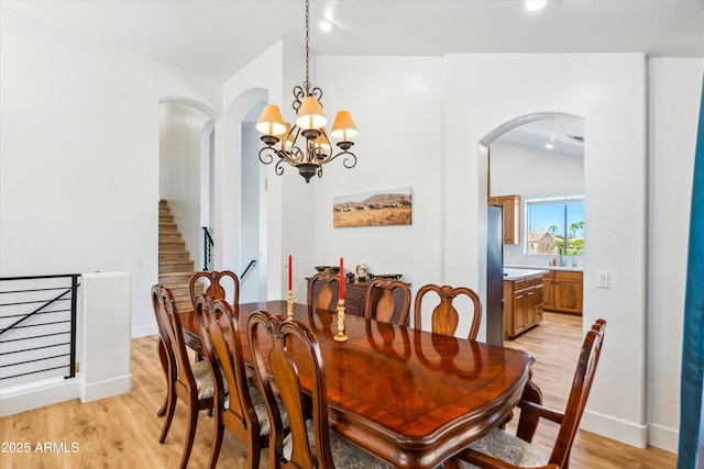 dining area with stairs, vaulted ceiling, arched walkways, and light wood finished floors