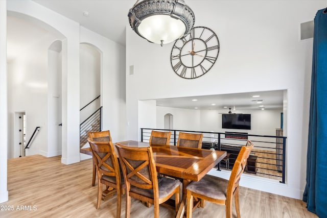 dining area with baseboards, light wood-type flooring, a towering ceiling, and arched walkways