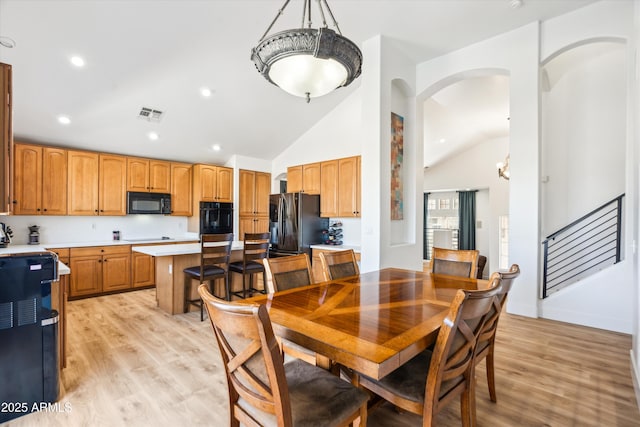 dining room featuring light wood finished floors, stairway, visible vents, and lofted ceiling