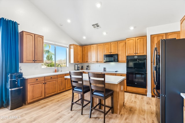 kitchen with black appliances, light wood-style flooring, a breakfast bar, a sink, and vaulted ceiling