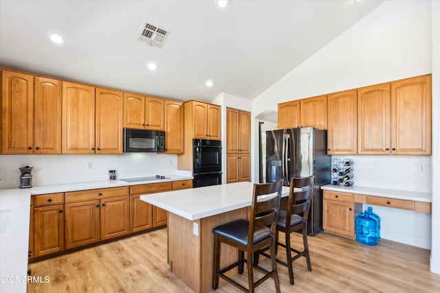 kitchen with visible vents, a breakfast bar, arched walkways, black appliances, and light countertops