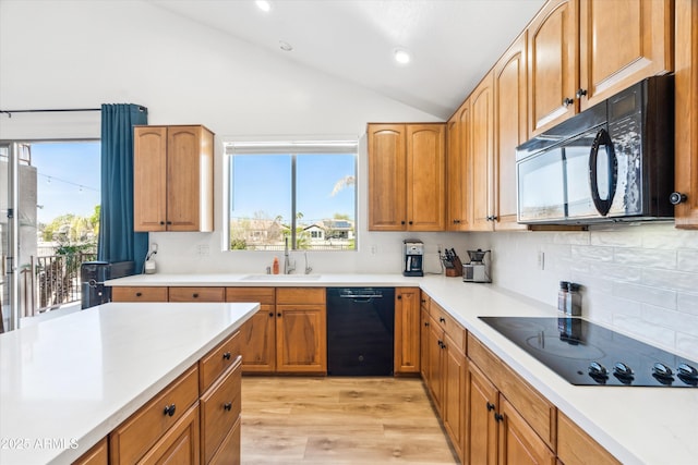 kitchen with a sink, lofted ceiling, black appliances, and light countertops