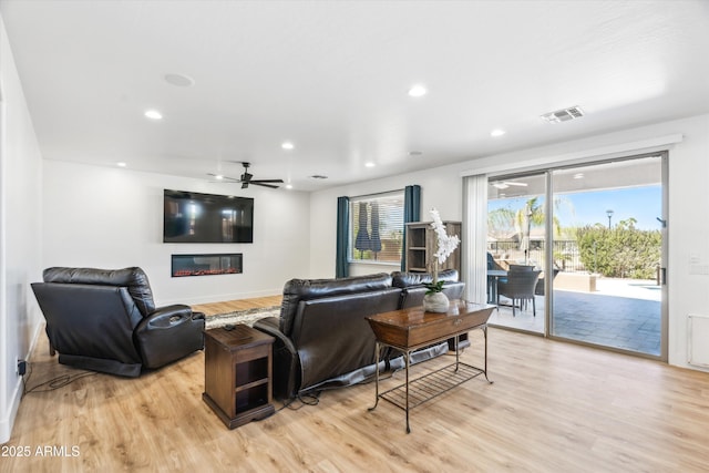 living room featuring a ceiling fan, visible vents, light wood finished floors, recessed lighting, and a glass covered fireplace