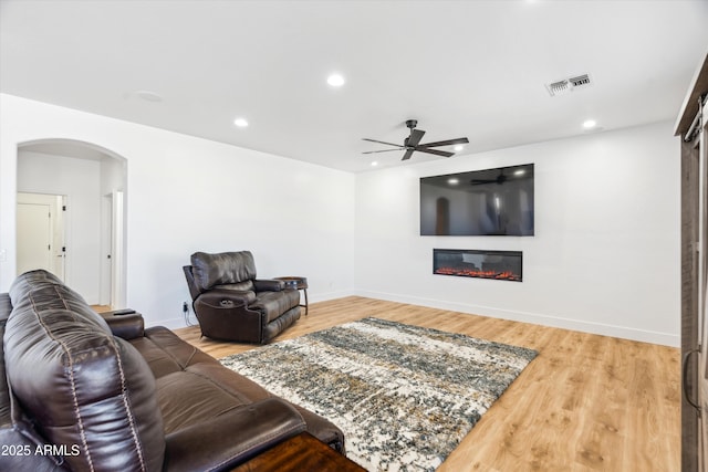 living room with visible vents, wood finished floors, a glass covered fireplace, arched walkways, and baseboards