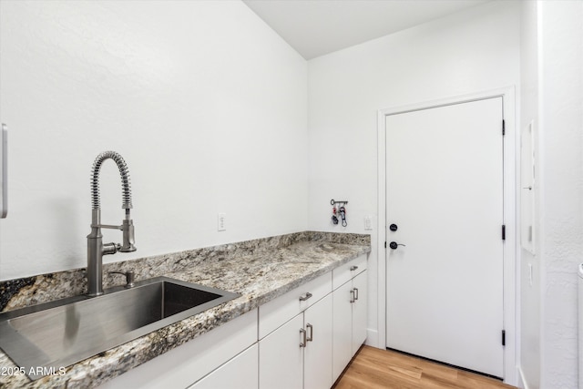 kitchen featuring white cabinets, light stone counters, light wood-style floors, and a sink