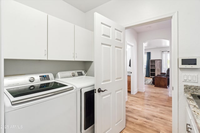 laundry room featuring arched walkways, cabinet space, light wood finished floors, baseboards, and washing machine and clothes dryer