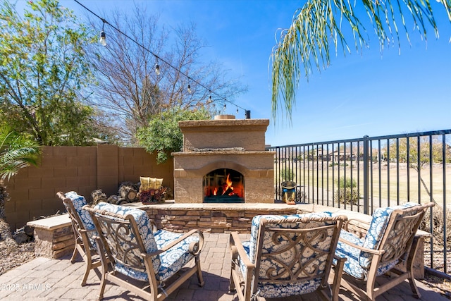 view of patio with fence and a warm lit fireplace