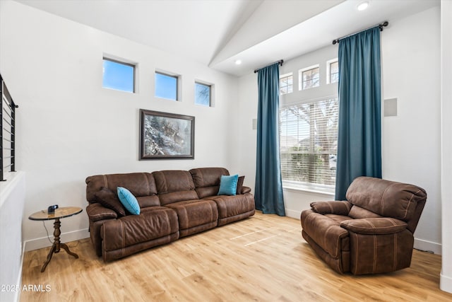 living area featuring a wealth of natural light, baseboards, vaulted ceiling, and light wood finished floors