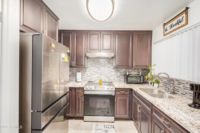 kitchen with tasteful backsplash, light stone counters, stainless steel appliances, under cabinet range hood, and a sink