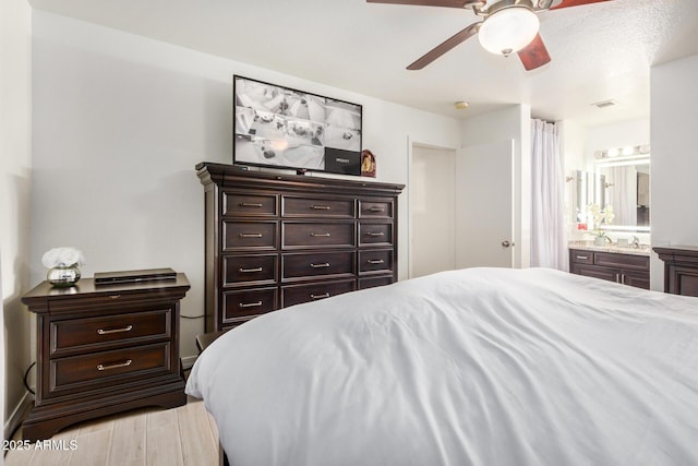 bedroom featuring visible vents, a ceiling fan, ensuite bath, and light wood-style flooring