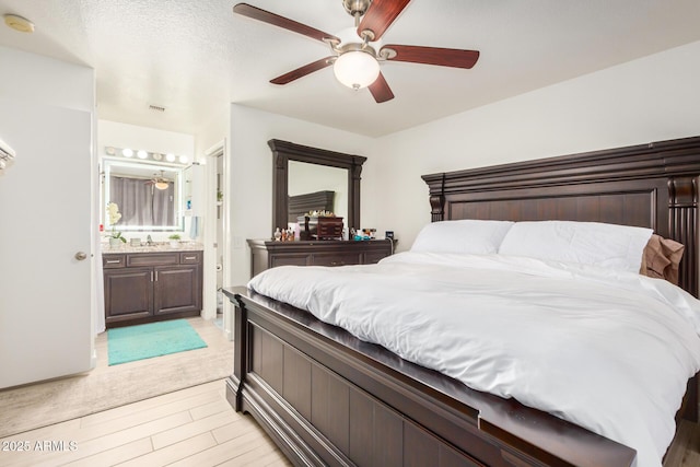 bedroom featuring a sink, a ceiling fan, visible vents, light wood-style flooring, and ensuite bathroom