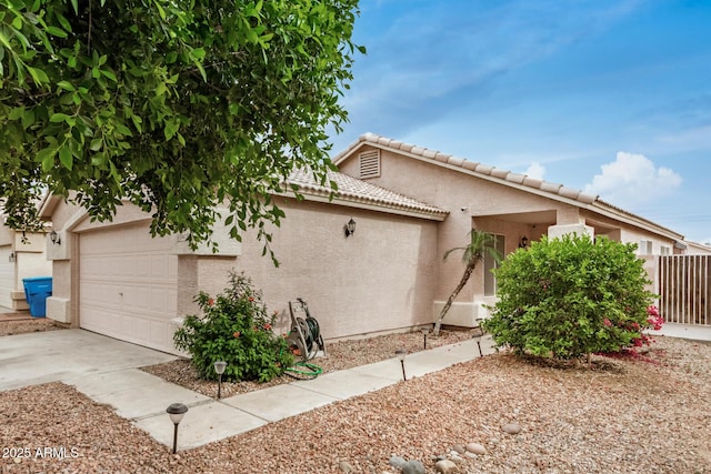 view of front of property featuring stucco siding, fence, a tile roof, driveway, and an attached garage