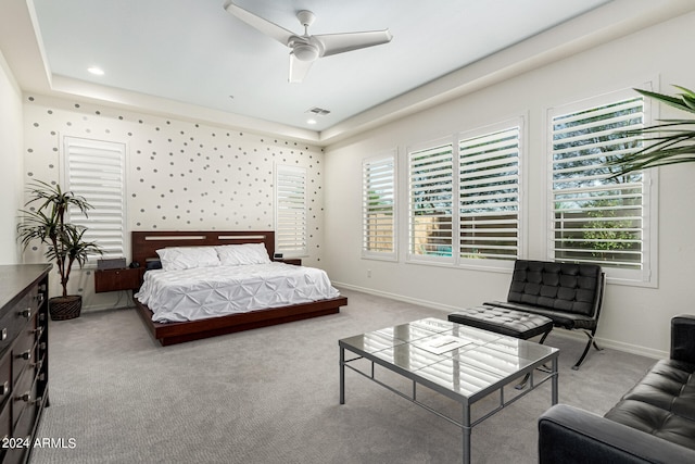 bedroom featuring ceiling fan, light carpet, a tray ceiling, and multiple windows