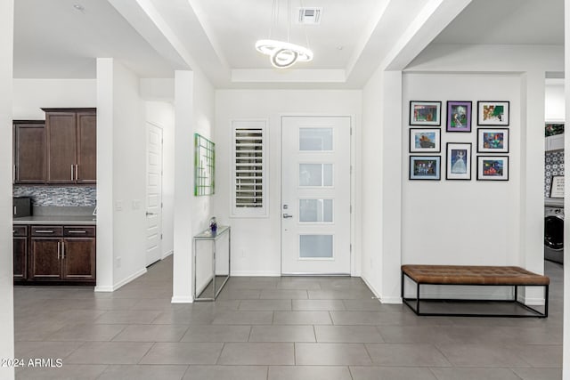 foyer featuring washer / clothes dryer, a raised ceiling, and dark tile patterned flooring