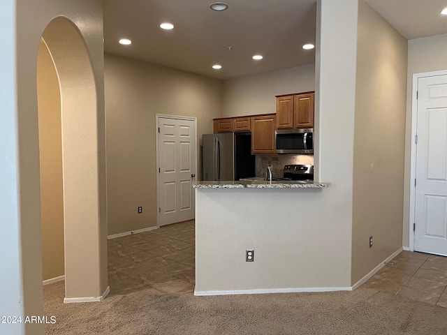 kitchen with light stone counters, light colored carpet, appliances with stainless steel finishes, and kitchen peninsula