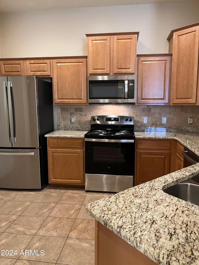 kitchen with appliances with stainless steel finishes, tasteful backsplash, sink, light stone counters, and light tile patterned floors