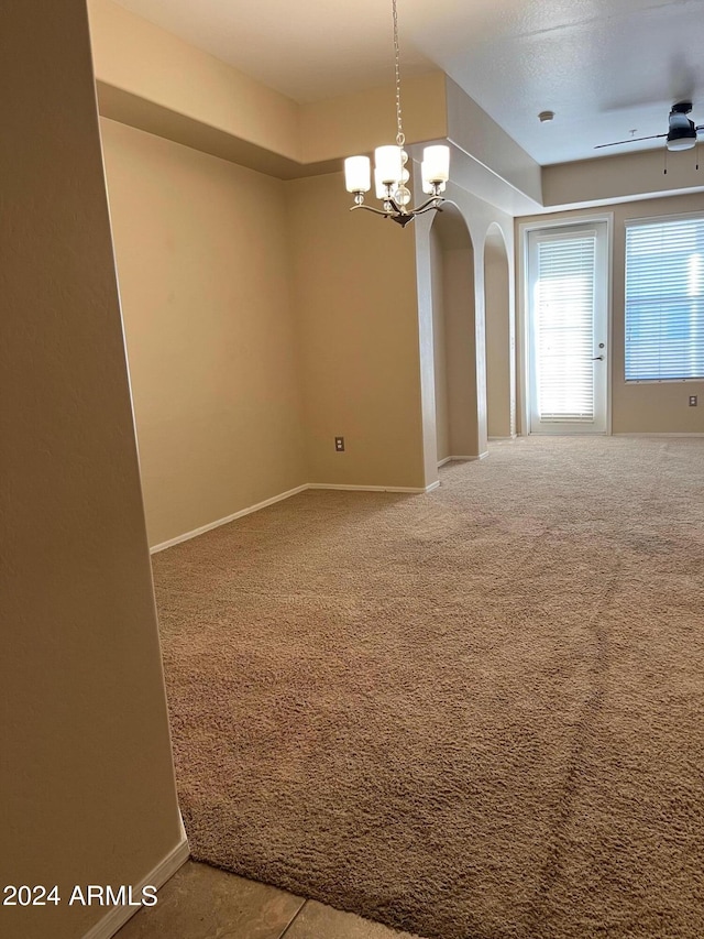 carpeted spare room featuring ceiling fan with notable chandelier