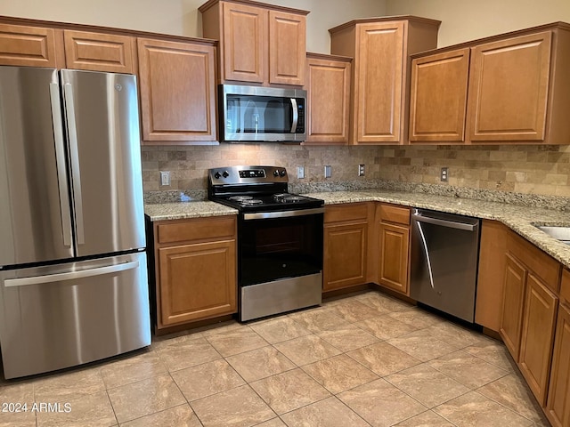 kitchen featuring light tile patterned flooring, backsplash, light stone countertops, and stainless steel appliances