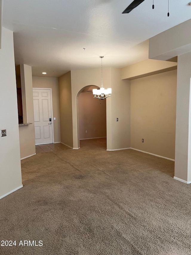 carpeted empty room featuring ceiling fan with notable chandelier