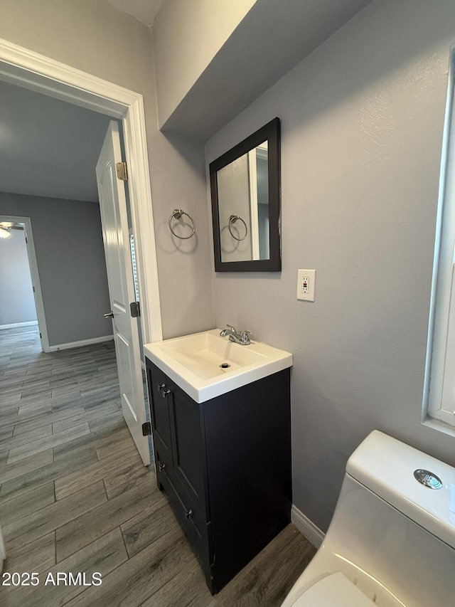 bathroom featuring toilet, baseboards, vanity, and wood finished floors